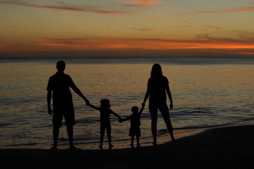 Silhouette of a family holding hands on a beach at sunset, symbolizing togetherness, intentional parenting, and the beauty of shared moments in nature. Helping fathers see how to leave a legacy with intentional fatherhood retreats.