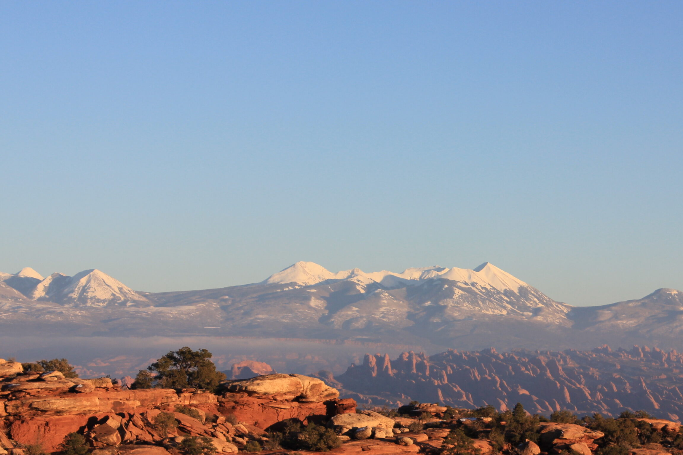Scenic landscape with snow-capped mountains under a clear blue sky, framed by red rock formations and desert vegetation—symbolizing contrast, resilience, and the journey toward intentional living.